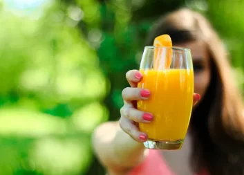 Mujer mostrando un vaso de vidrio con jugo o zumo de naranja natural al aire libre llena de salud y bienestar