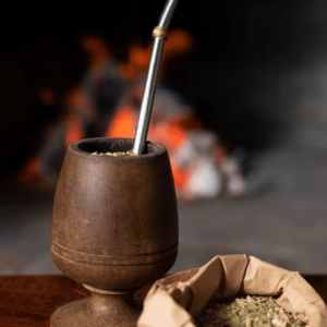 Mate de madera sobre una mesa de madera y su yerba mate con sus beneficios.